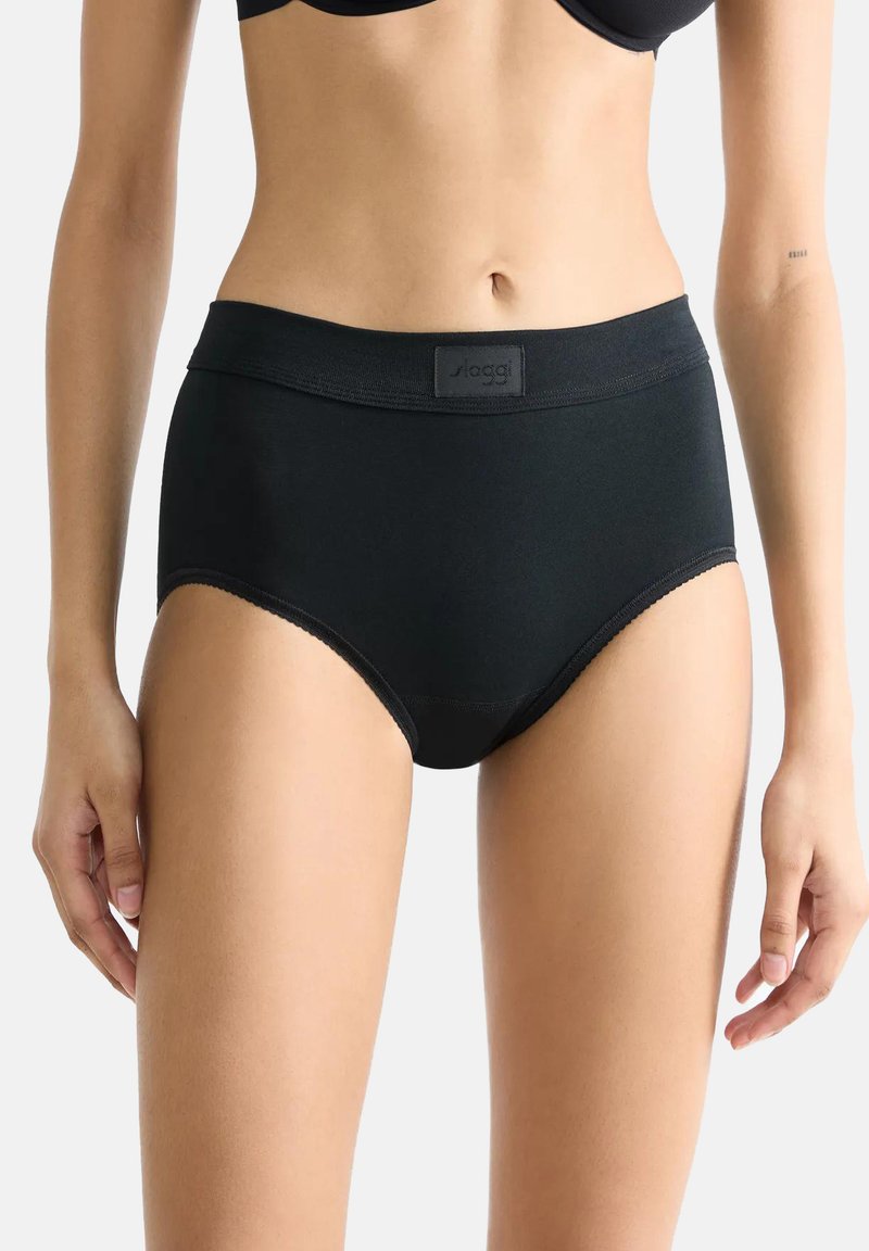 Femme portant un slip noir taille haute avec une large ceinture élastique et un logo de marque subtil au centre devant, visible de la moitié du torse jusqu'aux cuisses supérieures.