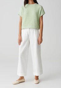 Lys grøn ribbet strikket cropped top parret med løse hvide bukser. Bukserne har foldede manchetter, og skoene er beige slip-on.