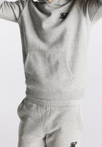 Grau Baumwoll-Hoodie mit einer Fronttasche und gerippten Bündchen, ausgestattet mit einem schwarzen Logo auf der Brust, kombiniert mit passenden Jogginghosen.