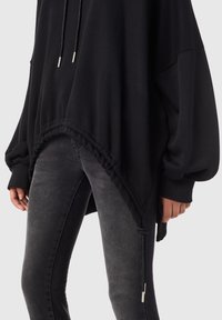 Svart oversized sweatshirt med dragsko, med ribbade ärmslut, texturerad tyg och en rynkad nederkant. Matcher med mörkgrå jeans.