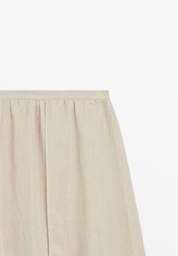 Beige linnen rok met geplooide taille en gladde A-lijn silhouet tegen een witte achtergrond.