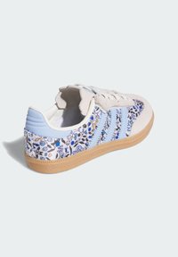 Blumenmuster-Sneaker mit hellblauen Akzenten, beigem Wildleder und einer Gummisohle. Verfügt über drei blaue Streifen und strukturierte Details.