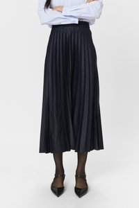 Svart plisserad kjol i mjukt tyg, med hög midja och flödande design, i kombination med svarta pumps med spetsig tå och genomskinliga strumpor.
