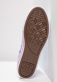 Fioletowa podeszwa trampka z płótna, z teksturowanym brązowym wzorem gumowym, białą zewnętrzną krawędzią i różowymi akcentami wzdłuż krawędzi. Posiada klasyczny detal z logo.