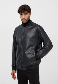 Czarna skórzana kurtka bomberka z zamkiem z przodu, ściągaczem na kołnierzu i mankietach oraz kieszeniami bocznymi, o gładkiej fakturze i luźnym kroju.