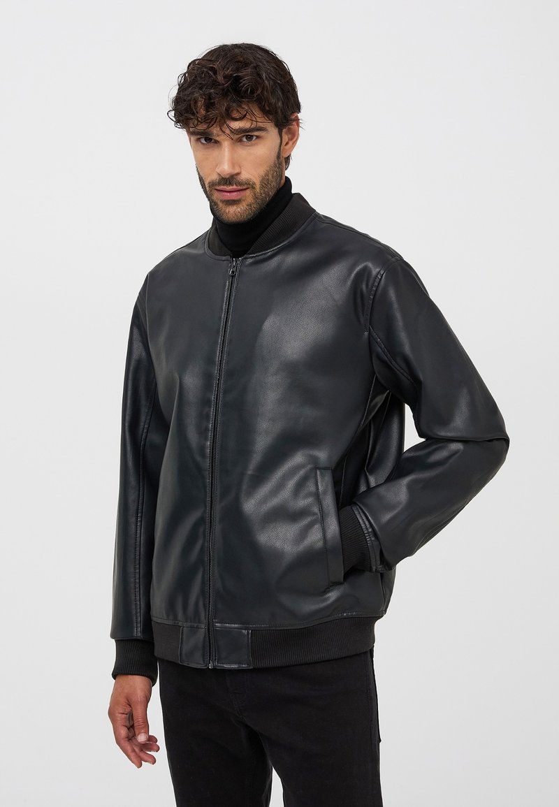 Czarna skórzana kurtka bomberka z zamkiem z przodu, ściągaczem na kołnierzu i mankietach oraz kieszeniami bocznymi, o gładkiej fakturze i luźnym kroju.