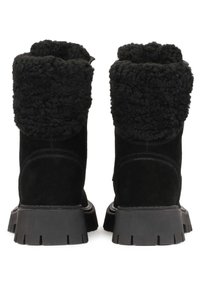 Botines de ante negros con un puño de piel de oveja negra esponjosa, superficie texturizada, y una suela de goma negra resistente con un dibujo en el patrón.