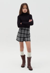Suéter negro de cuello alto, pantalones cortos de cuadros en blanco y negro, calcetas crema hasta la rodilla y botas de cuero marrón. Diseño simple y moderno.