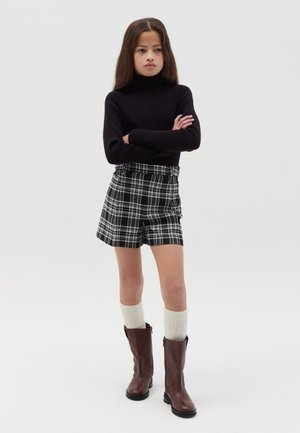 Zwarte coltrui, geruite shorts in zwart en wit, kniehoog crèmekleurige sokken en bruine leren laarzen. Eenvoudig en modern ontwerp.