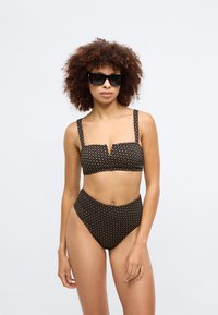 Svart bikini med et mønstret tekstur, som har en cropped topp med firkantet halsringning og høyhøyde underdeler. Modellen har på seg svarte solbriller.