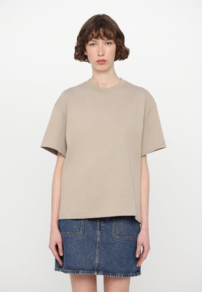 Μπεζ oversized μπλουζάκι με κοντά μανίκια, στρογγυλή λαιμόκοψη και μαλακή υφή, σε συνδυασμό με μπλε τζιν φούστα με τσέπες.