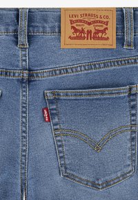 Ljust blå denimjeans med gula sömmar, som har en brun läderetikett vid midjan och en liten röd flagga på sidofickan.