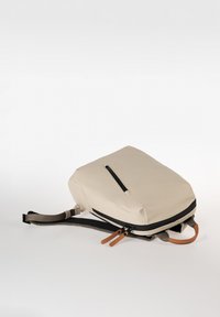 Zaino beige con una texture liscia, forma rettangolare, tasca frontale con zip e dettagli in pelle sui tiranti della zip. Incluso cinturino regolabile.