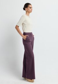 Haut ivoire à manches courtes avec embellissement floral au col, associé à un pantalon plissé prune taille haute et des escarpins beiges.
