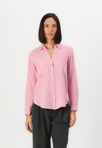 Pink button-up shirt with a textured pattern, featuring a collar, two chest pockets, and long sleeves. Worn with gray trousers.
