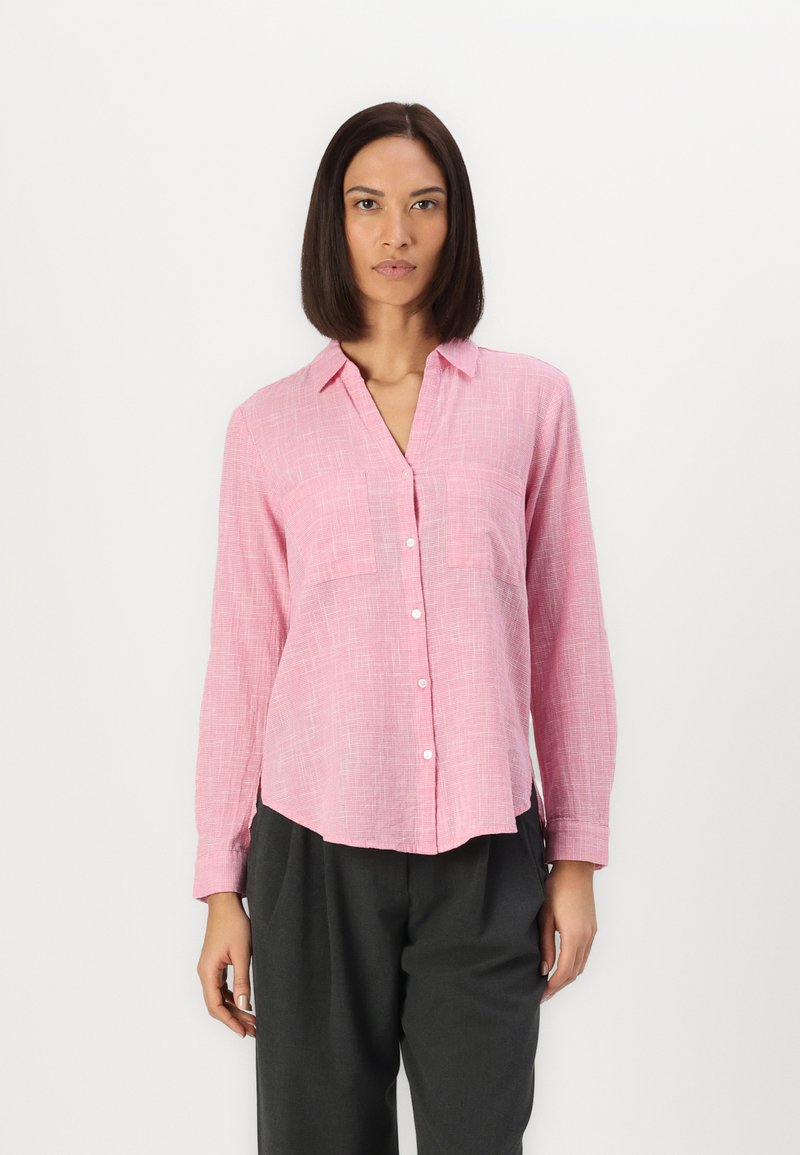 Pink button-up shirt with a textured pattern, featuring a collar, two chest pockets, and long sleeves. Worn with gray trousers.