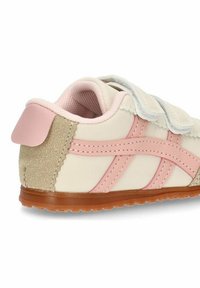 Zapatilla deportiva infantil en color beige claro con detalles en rosa y correas grises. Presenta un talón de textura rugosa y una suela flexible de goma marrón.