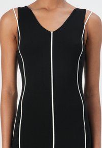 Black knit dress featuring a V-neck, thin white accent lines down the front, and slender straps. Smooth texture with a fitted silhouette.