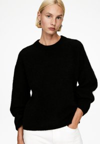 Schwarzer Strickpullover mit rundem Halsausschnitt, lockerer Passform und leicht gepufften Ärmeln. Der Stoff wirkt weich und strukturiert.