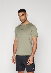Olivengrønn kortermet treningstrøye med rund hals og svart Nike-logo. Båret med svarte treningsshorts med hvit logo.
