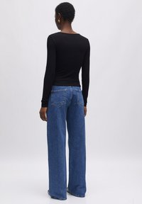 Zwarte langemouwen fitted top gecombineerd met wijde, blauwe jeans met een hoge taille en achterzakken. De stof ziet er glad en zacht uit.