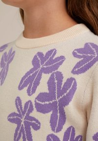 Pleteni pulover v krema barvi z velikim vijoličnim cvetličnim vzorcem, z okroglim izrezom in rahlo teksturirano tkanino.