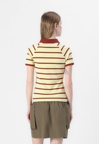 Gulstripe polo-skjorte med maroon-detaljer, kortermet og ribbet krage, sammen med en khaki skjørt med sidelommer.