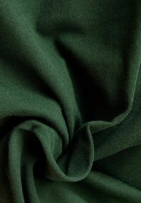 Tessuto verde scuro con una texture liscia e lavorata a maglia, caratterizzato da pieghe drappeggiate che ne accentuano l'aspetto morbido. Nessun motivo o hardware in evidenza.
