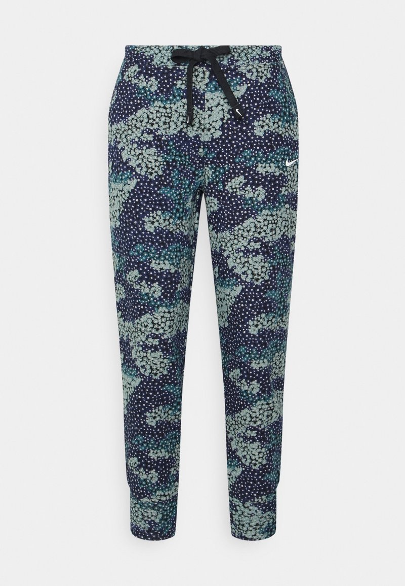 Pantalon de jogging bleu marine avec motif floral abstrait vert et blanc, taille à cordon noir et petit logo Nike blanc sur la cuisse droite.