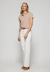 Pikétröja i ljusrosa bomull med knäppt krage, kombinerad med vita vida jeans och ljusbruna klacksandaler.