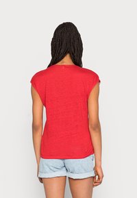 T-shirt rosso a maniche corte con vestibilità morbida e tessuto morbido, abbinato a pantaloncini in denim chiaro. Presenta un collo a giro e dettagli minimi.
