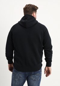 Zwarte hoodie met een gladde textuur, raglanmouwen en een kangoeroezak. Heeft een effen achterkant en geribbelde manchetten en zoom.