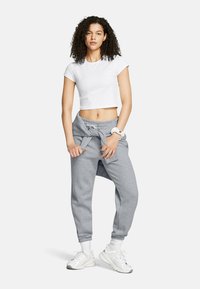 Grijze sweatpants met een koord in de taille, gecombineerd met een cropped wit t-shirt. Witte sneakers en een haarband om de pols maken de look compleet.