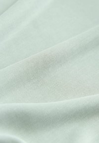 Tissu vert clair avec une surface lisse et légèrement texturée, présentant un léger étirement et un motif de tissage fin.