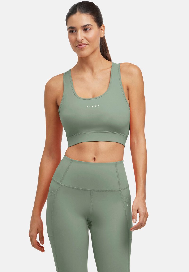 Oliwkowy sportowy biustonosz i legginsy z wysokim stanem, wykonane z gładkiego, elastycznego materiału. Biustonosz ma logo z przodu, minimalistyczny design i szerokie ramiączka.