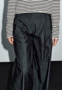 Zwarte denim broeken met plooien en een relaxte pasvorm, gecombineerd met een zwart-witte gestreepte longsleeve shirt. Gladde textuur, minimalistisch design.