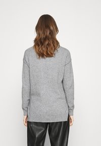 Maglione grigio a maglia con una vestibilità comoda, polsini e orlo a coste, con spacchi laterali per maggior comfort. Indossato sopra pantaloni in pelle nera.
