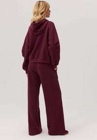 Burgundowy hoodie z kapturem i luźnym krojem, połączony z dopasowanymi spodniami z szerokimi nogawkami. Wykonany z miękkiego, teksturowanego materiału dla wygody.