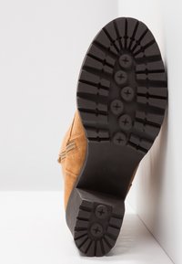 Bottine en daim marron avec une semelle épaisse en caoutchouc noir, présentant un motif de bande de roulement texturé pour l'adhérence et une fermeture éclair sur le côté.