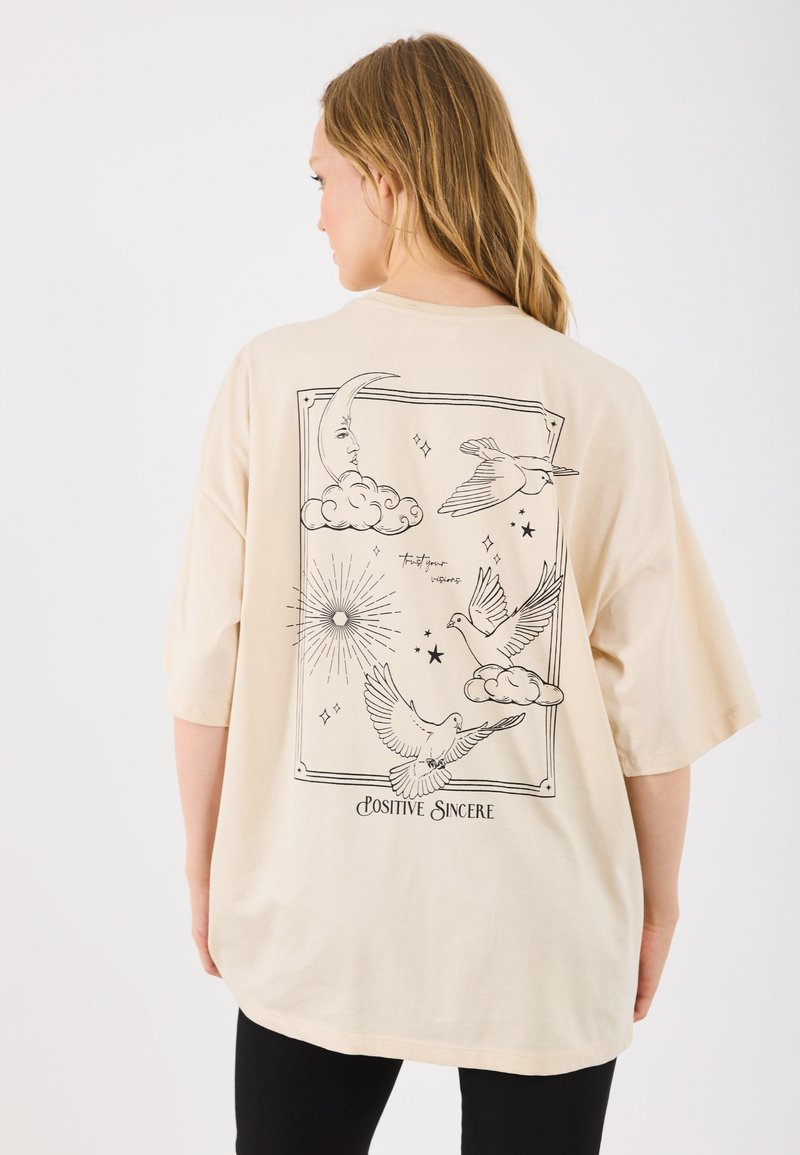 Beige oversized t-shirt met zwarte grafische ontwerpen van vogels, wolken, een maan en de tekst "Positive Sincere" op de achterkant.