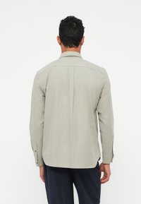 Camisetta grigia chiara a maniche lunghe con tessuto strutturato, polsini con bottone e una piega posteriore, caratterizzata da un design con colletto classico.