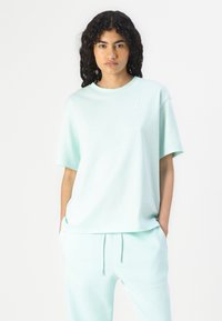 Licht mintgroene katoenen T-shirt met korte mouwen en een ronde hals, voorzien van een klein wit logo op de borst.