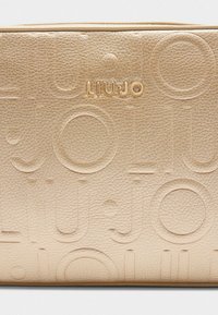 Geantă din piele artificială aurie, cu design logo embossat. Textură netedă și formă rectangulară, având un luciu subtil și închidere cu fermoar.