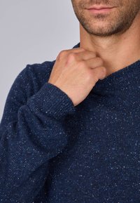 Pull marine en laine texturée, avec un col rond et des poignets côtelés, présentant des motifs mouchetés pour une touche de détail supplémentaire.