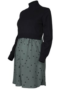 Czarna swetrowa bluzka typu golf z długimi rękawami, w połączeniu z zieloną sukienką w kropki z guzikami i bocznymi rozcięciami.