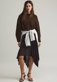 Bruin pluizig vest, lichtblauw gestreept overhemd in de taille gestrikt, asymmetrische zwarte mesh rok, zwarte sandalen met hoge hak.