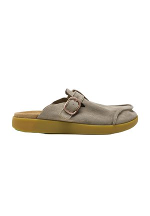 Zapato beige de ante tipo slip-on con punta redondeada, correa ajustable con hebilla y gruesa suela de goma marrón.