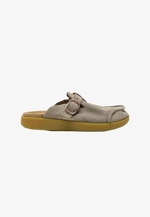Zapato beige de ante tipo slip-on con punta redondeada, correa ajustable con hebilla y gruesa suela de goma marrón.