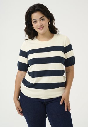 Pull en maille à rayures, à manches courtes, en crème et marine. Encolure ronde, texture douce et coupe décontractée. Associé à un jean bleu foncé.