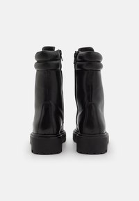 Botas de cuero negro hasta el tobillo con un acabado suave, que presentan un cierre de cremallera y un collarín acolchado, montadas sobre una suela de goma gruesa y texturizada.